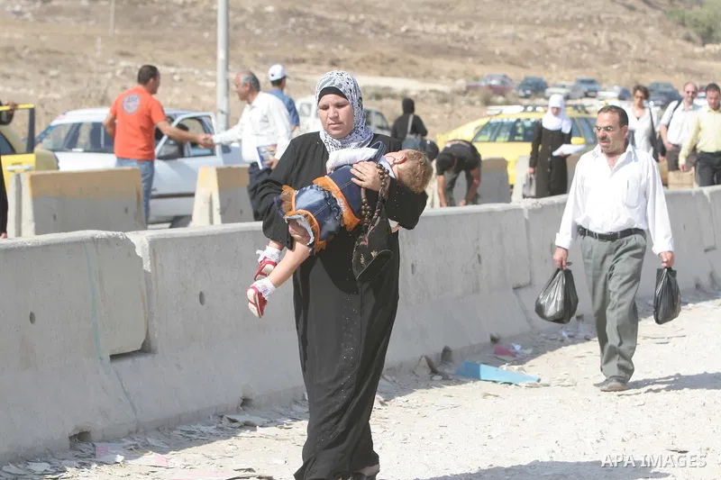 A Palestinian woman carry her baby and cross the Hawara checkpoint near the West Bank city of Nablus. The Israeli military announced an open-ended closure of the West Bank and Gaza Strip Wednesday, ahead of the weeklong...