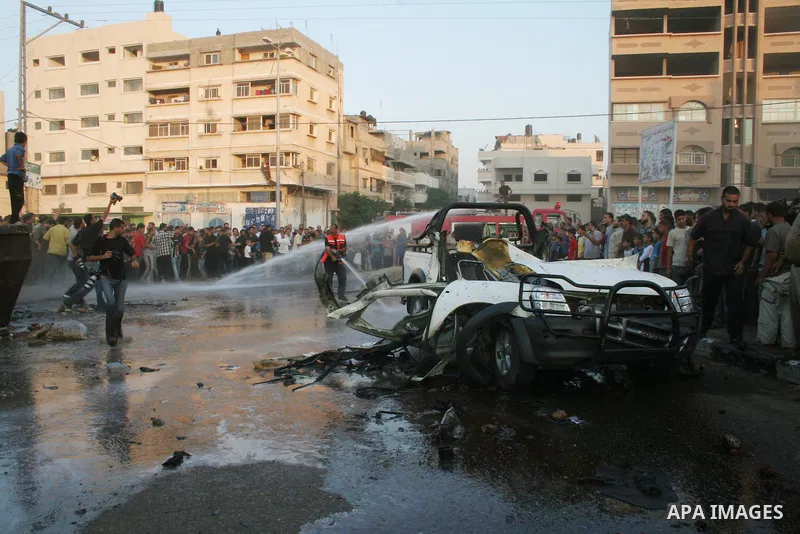 Water is sprayed as Palestinians gather around the wreckage of a car after it was hit in an Israeli missile strike in the Zeitoun neighborhood of Gaza City. Israel killed four Gaza militants in a missile strike on a jeep...