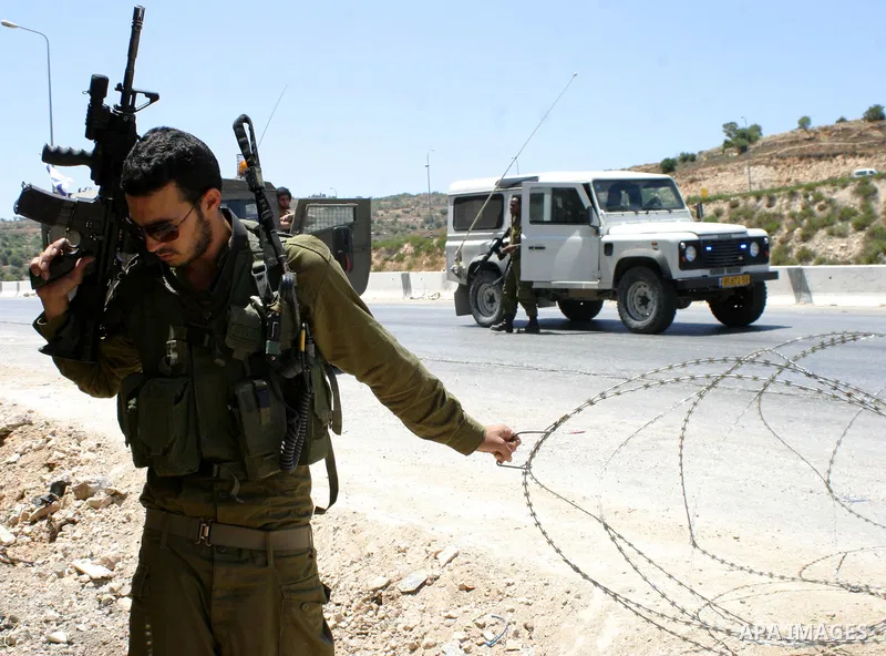 Israeli soldiers stand on guard behind barbed wire as they restrain Palestinian and foreign demonstrators during a protest against the construction of the controversial separation barrier in the village of Al-Khader near...