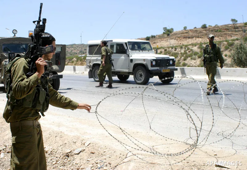 Israeli soldiers stand on guard behind barbed wire as they restrain Palestinian and foreign demonstrators during a protest against the construction of the controversial separation barrier in the village of Al-Khader near...