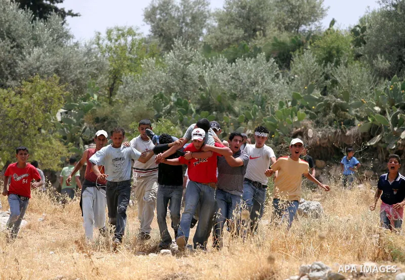 Palestinian youth carry a wounded comrade during a demonstration against Israel's controversial separation barrier in the West Bank village of Nilin, near Ramallah. Five Palestinians were wounded today as Israeli soldier...