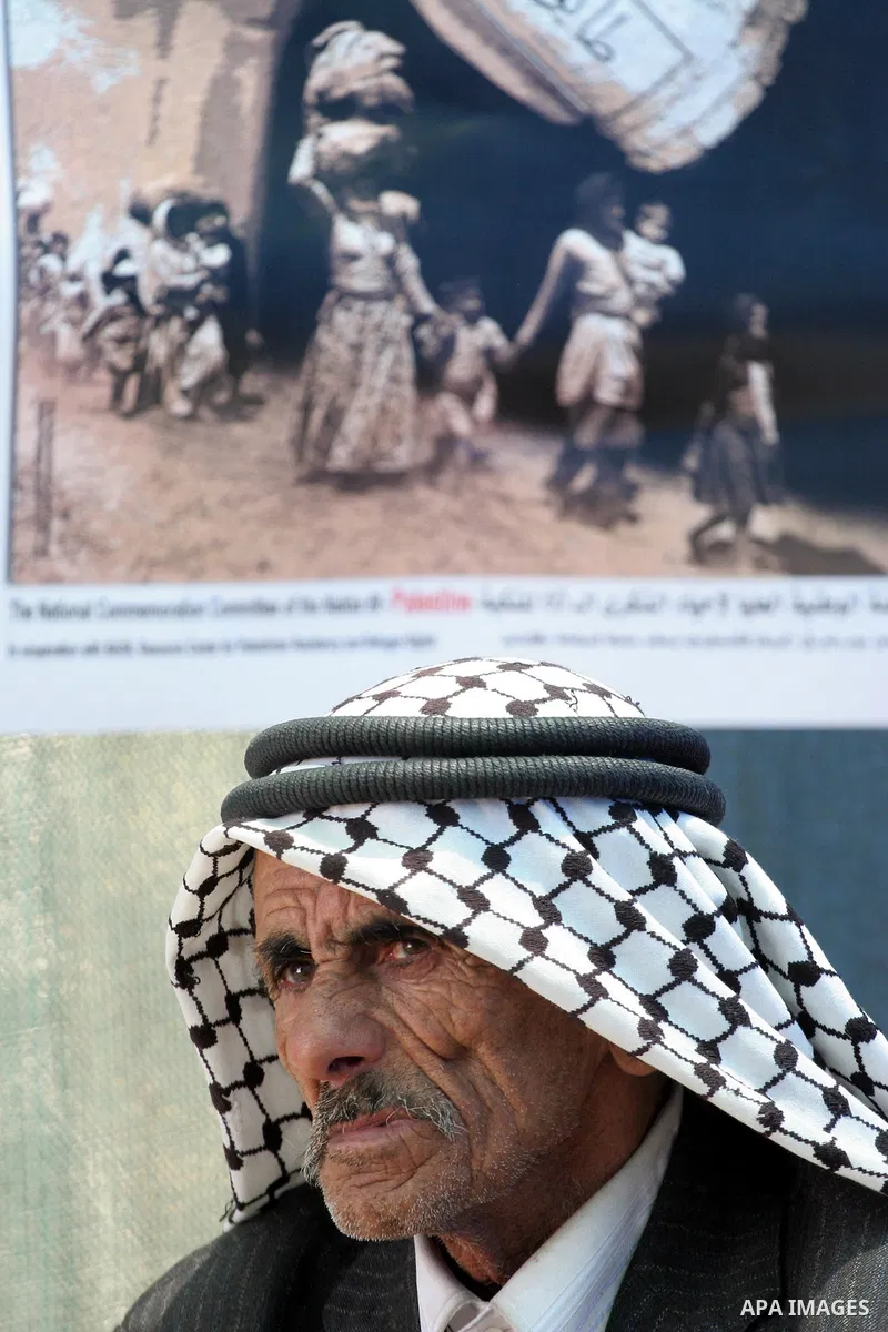 An elderly Palestinian man sits Under a poster commemorating the Nakba, or the catastrophe, the Arabic term used to describe the uprooting of hundreds of thousands of Palestinians with the 1948 creation of the state of I...
