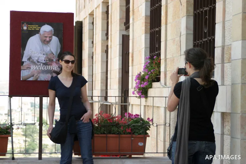 A Christian worshipper takes a picture next a portrait of Pope Benedict XVI outside the Church of the Nativity, traditionally believed to be the birthplace of Jesus Christ, in the West Bank city of Bethlehem, on May 11,...