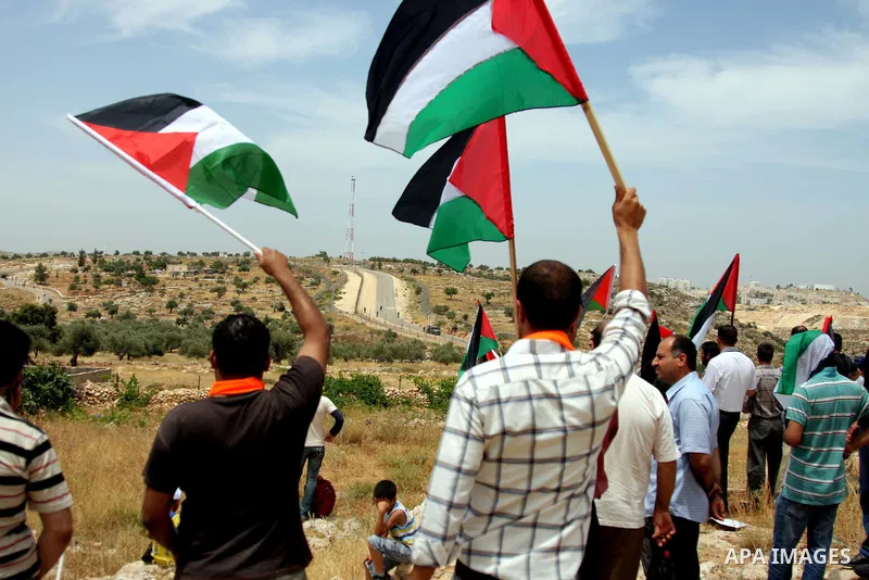 Palestinians holding his national flag walks past a banner that reads in Arabic and English "Obama have a look, 42 years of occupation" during a demonstration in the West Bank city of Bilin, near Ramallah, on June 4,2009...