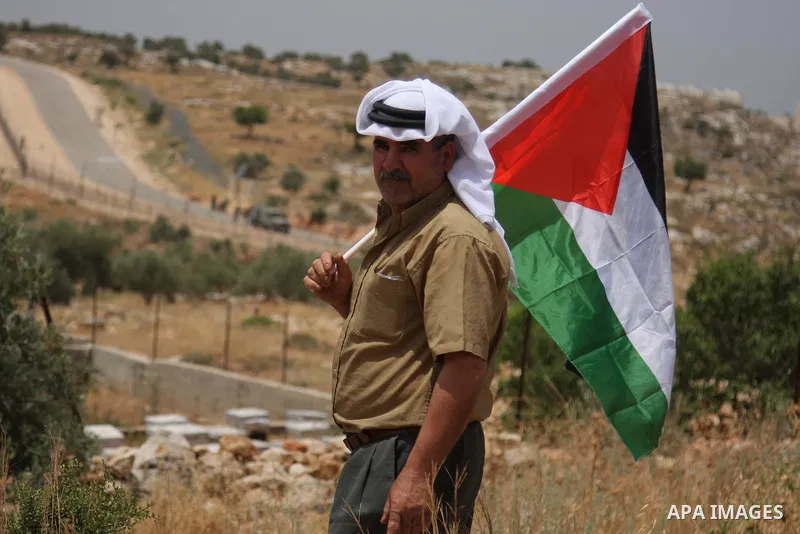 Palestinians holding his national flag walks past a banner that reads in Arabic and English "Obama have a look, 42 years of occupation" during a demonstration in the West Bank city of Bilin, near Ramallah, on June 4,2009...