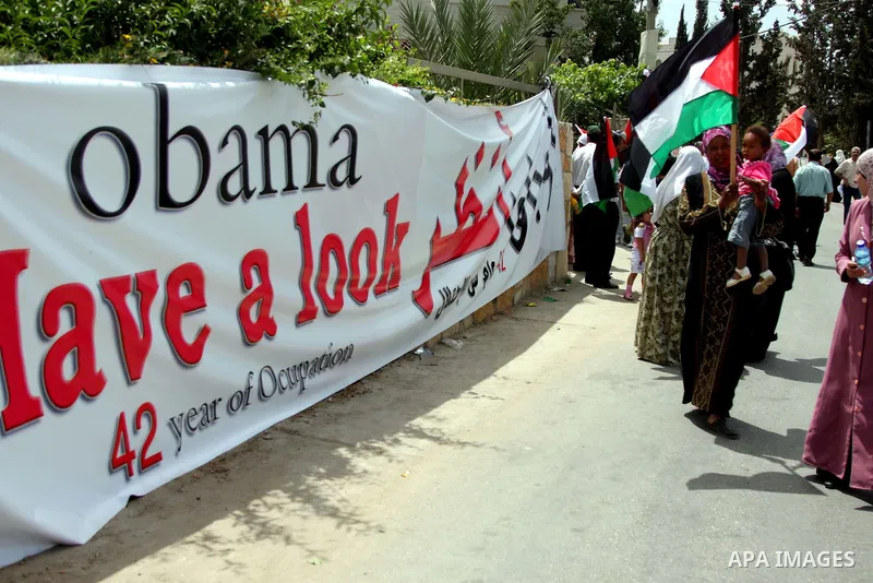 Palestinians holding his national flag walks past a banner that reads in Arabic and English "Obama have a look, 42 years of occupation" during a demonstration in the West Bank city of Bilin, near Ramallah, on June 4,2009...
