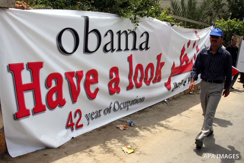Palestinians holding his national flag walks past a banner that reads in Arabic and English "Obama have a look, 42 years of occupation" during a demonstration in the West Bank city of Bilin, near Ramallah, on June 4,2009...