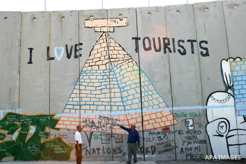 Palestinian men are pointing at a paint on the controversial Israeli barrier in the West Bank town of Bethlehem on July 6 2009. Photo by Najeh Hashlamoun