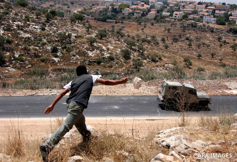 Palestinian youths throw stones at an Israeli military vehicle during a protest against the construction of the West Bank separation barrier in the village of Nilin near Ramallah on July 8, 2009. Photo by Issam Rimawi