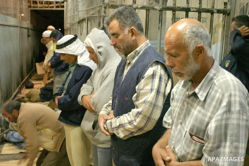 Palestinian workers pray as others line-up they wait to cross a checkpoint to work in Israel at the separation barrier in the West Bank town of Bethlehem, early 14 July 2009. As they head to work in Israel. According to...