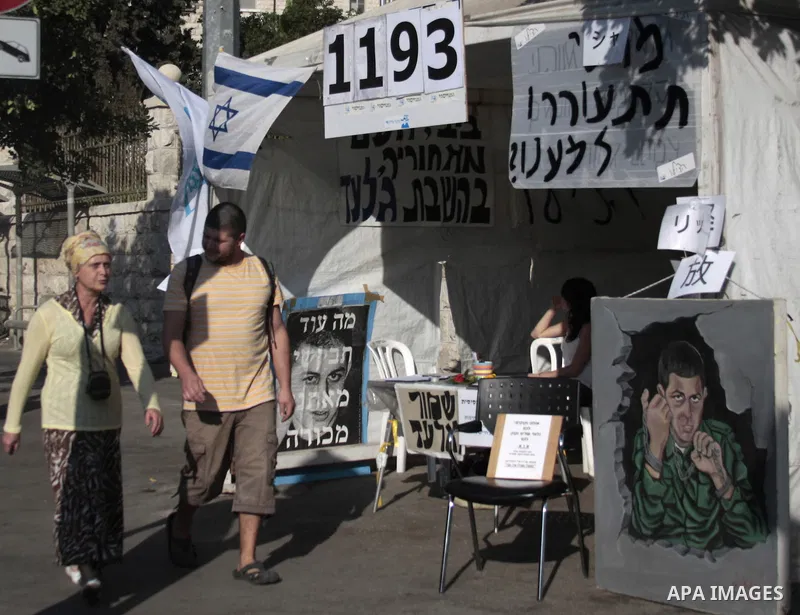 Pedestrians walk past a banner, depicting captured Israeli soldier Gilad Shalit, hung outside a protest tent calling for his release, near the residence of Israel's Prime Minister Benjamin Netanyahu in Jerusalem Septembe...