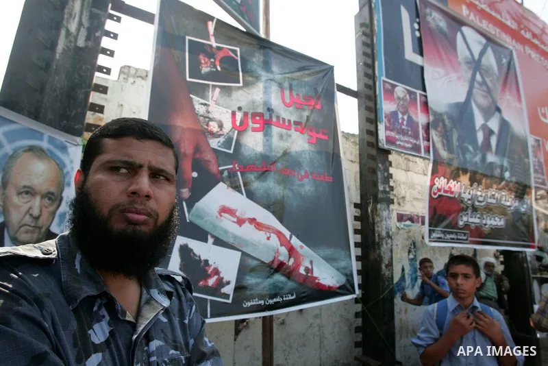 A hamas policeman stand near a poster of Palestinian president Mahmud Abbas with a phrase reading in Arabic, "to the dust bin of history, traitor" are plastered in a street in Gaza City on October 7, 2009. Hamas warned t...