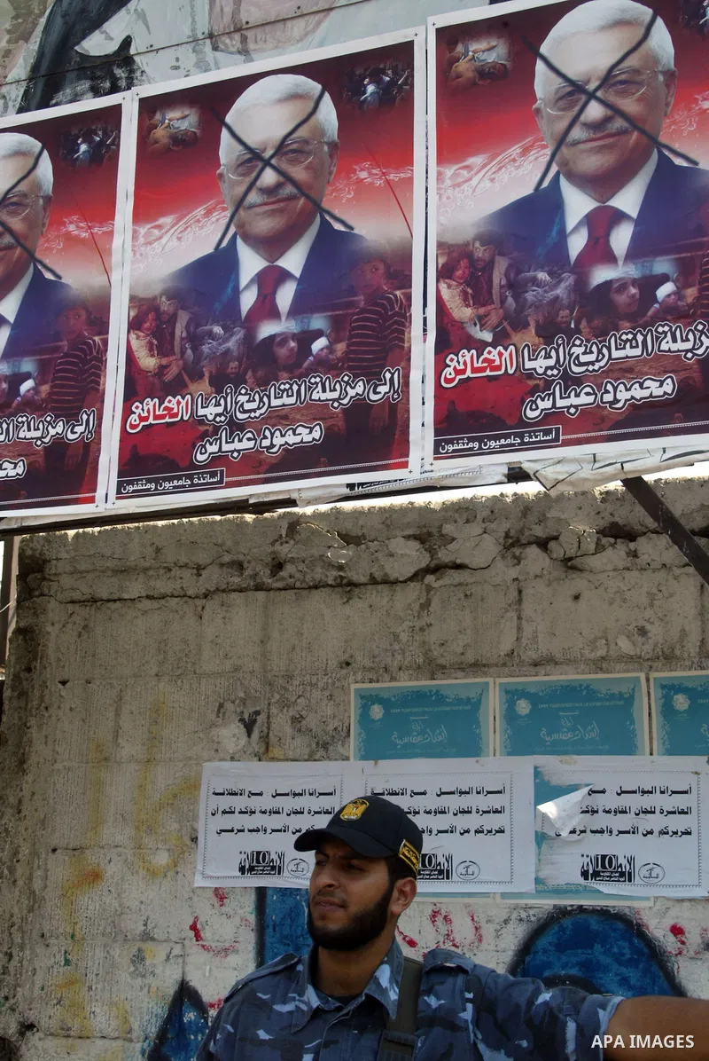 A hamas policeman stand under a poster of Palestinian president Mahmud Abbas with a phrase reading in Arabic, "to the dust bin of history, traitor" are plastered in a street in Gaza City on October 7, 2009. Hamas warned...