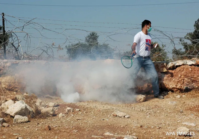 A Palestinian protestor uses a tennis racket to toss a used tear gas canister at Israeli soldiers during a demonstration against Israel's separation barrier in the West Bank village Billin near Ramallah on Oct 23, 2009....