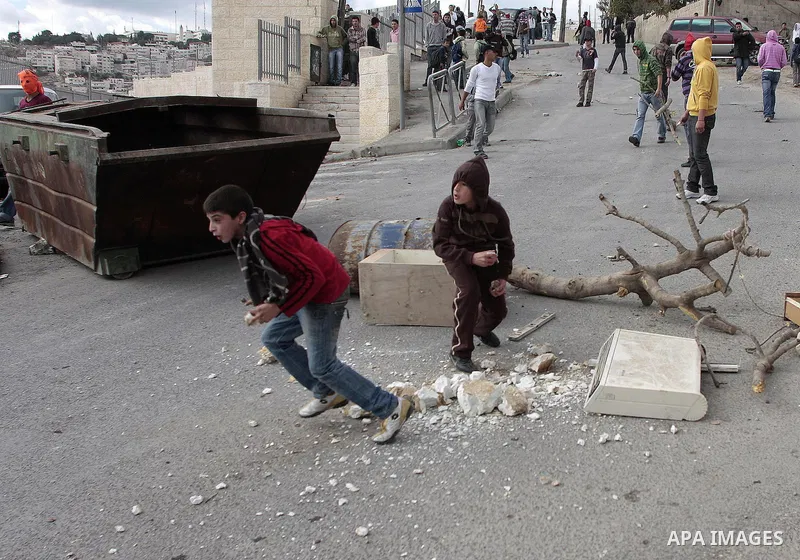 A Palestinian youths hurl stones at Israeli forces while an Israeli army bulldozer nearby demolishes a Palestinian house that was built without municipality permission in the Jerusalem Arab neighborhood of Isawiyya on No...