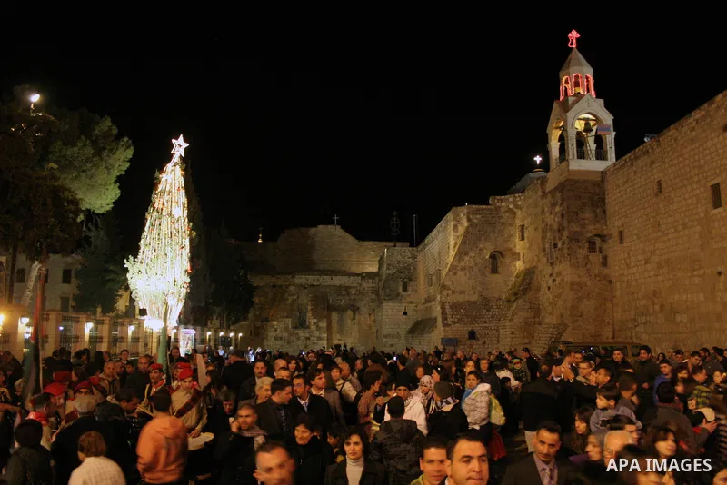 Palestinians gather around the lit Christmas tree outside the Church of the Nativity in the West Bank city of Bethlehem on December 15, 2009. Christians Pilgrims and tourists are expected to visit Bethlehem, the alleged...