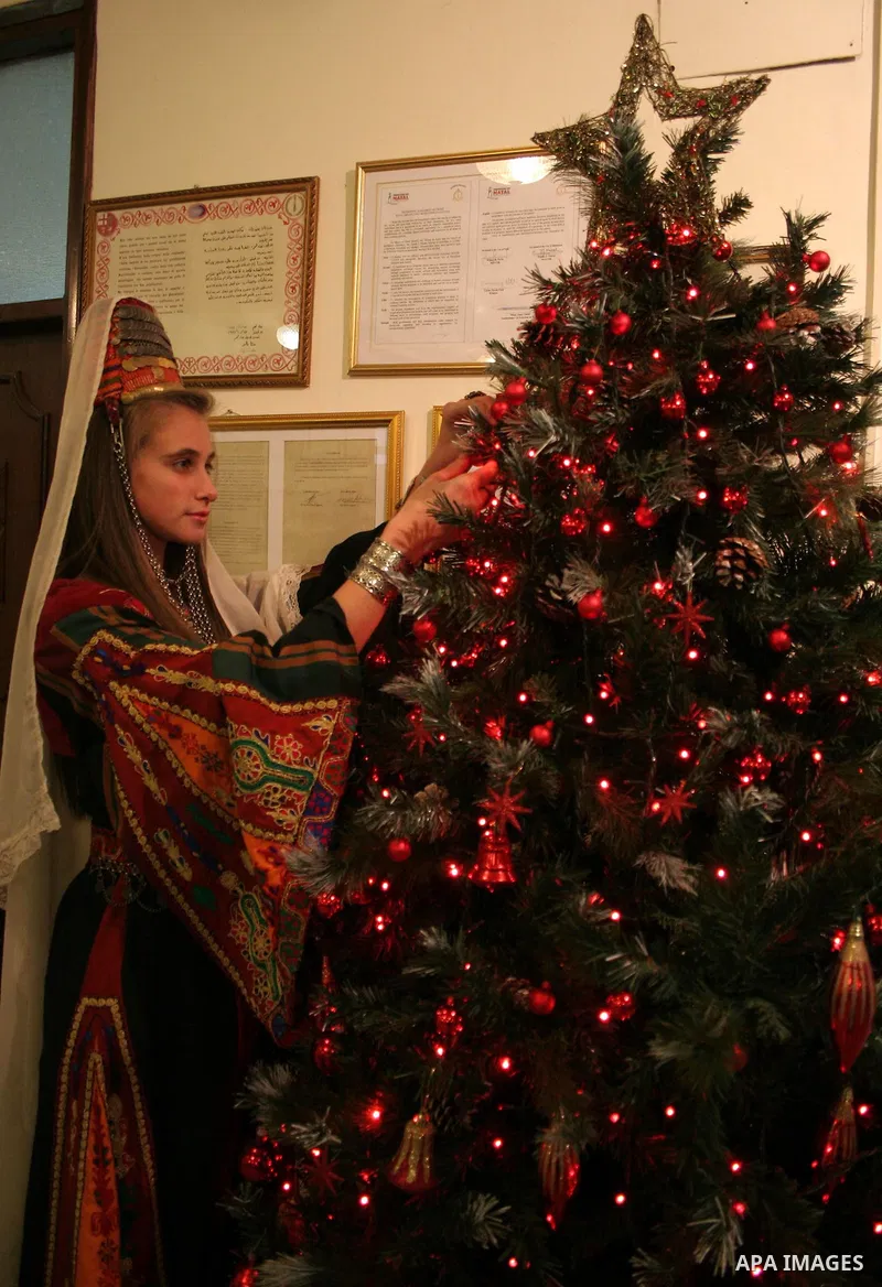 A Palestinian woman wearing traditional clothes decorates a Christmas tree inside the municipality building in the West Bank city of Bethlehem on December 15, 2009. Christians Pilgrims and tourists are expected to visit...