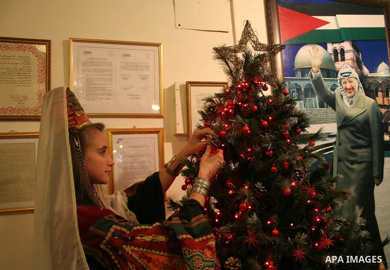 A Palestinian woman wearing traditional clothes decorates a Christmas tree inside the municipality building in the West Bank city of Bethlehem on December 15, 2009. Christians Pilgrims and tourists are expected to visit...
