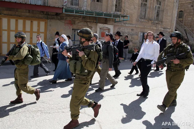 Israeli soldiers escort Jewish settlers as they head to visit the tomb of Atnaeil Ben Kinaz in the occupied West Bank city of Hebron on March 31, 2010. The United States wants a four-month Israeli building freeze in occu...