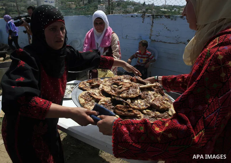 Palestinian women carry some of a huge portion of Musakhan, a traditional Palestinian dish made of chicken, flat bread, nuts and spices, on April 19, 2010 in the West Bank village of Arura, near Ramallah as they attempt...