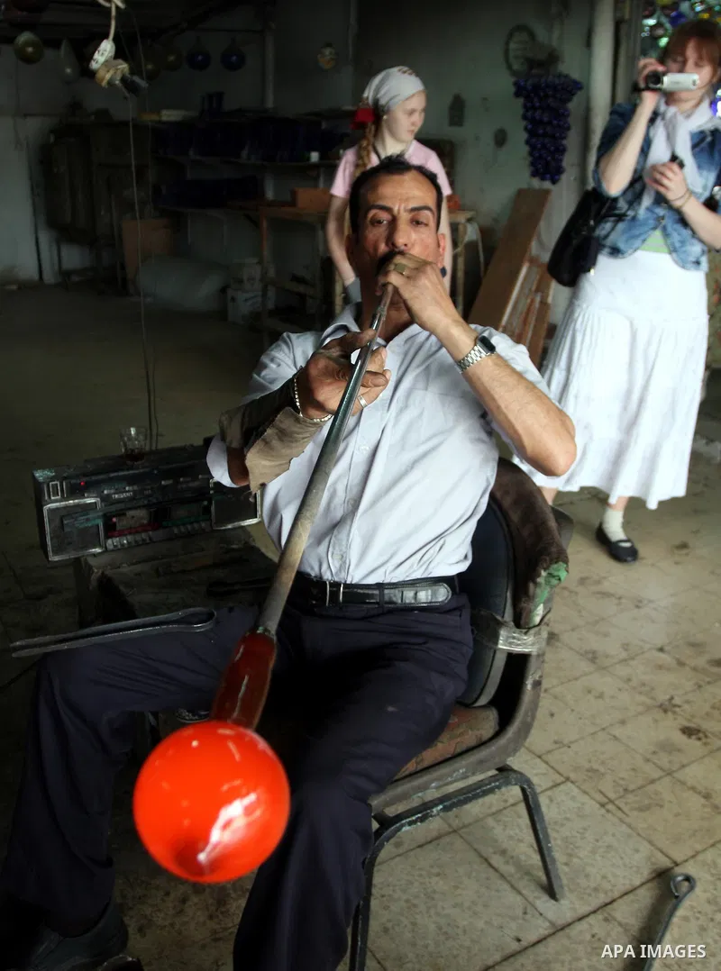 Foreign women look at a Palestinian worker as he makes a different types of glasses in AL-Salam factory in the West Bank city of Hebron on May 21, 2010. Glass has been a traditional industry in Hebron for over 600 years...