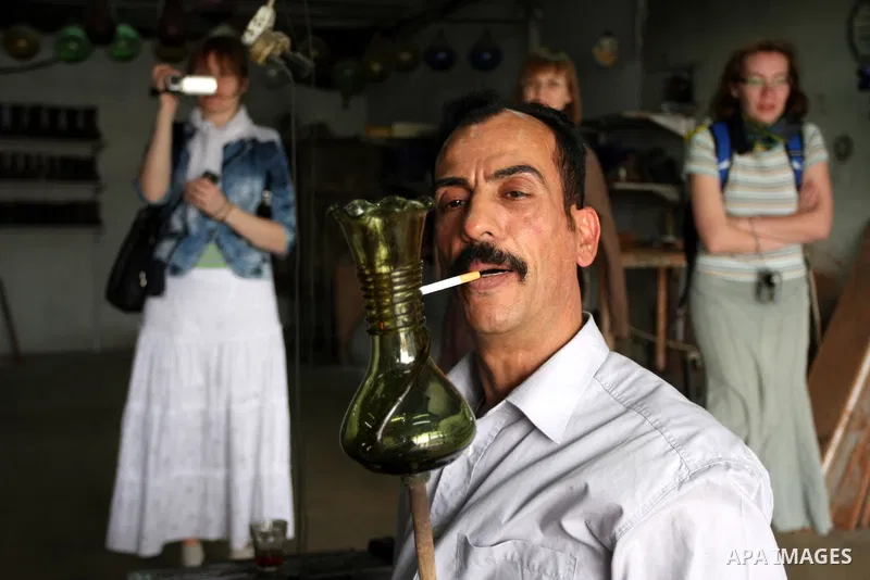 Foreign women look at a Palestinian worker as he makes a different types of glasses in AL-Salam factory in the West Bank city of Hebron on May 21, 2010. Glass has been a traditional industry in Hebron for over 600 years...