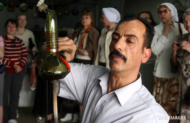 Foreign women look at a Palestinian worker as he makes a different types of glasses in AL-Salam factory in the West Bank city of Hebron on May 21, 2010. Glass has been a traditional industry in Hebron for over 600 years...