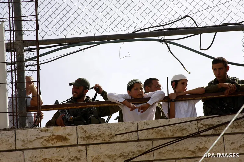 Israeli soldiers and children of jewish settlers look at Israeli left-wing activists and Palestinians as they protest against Jewish settlements and Shuhada street closing near Beit Romano settlement in the city center o...