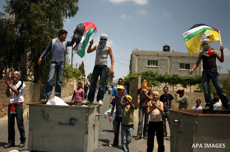 Palestinian men wave flags on dumpsters during clashes in the West Bank village of Nabi Saleh, on 28 May 2010. Palestinians protest weekly against the neighbouring Jewish settlement of Halamish. photo by Eyad Jadallah