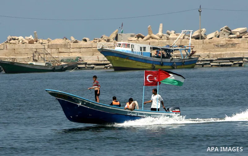 Palestinian fishermen ride a boat hold a Turkish flag and national flags in the port of Gaza City on May 31, 2010. At least 10 people were killed in an Israeli Navy raid on a fleet of aid ships, most of them Turkish nati...