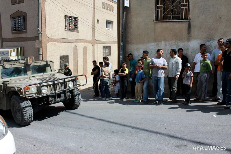 Palestinians stand near Israeli soldiers as they inspect a car which was burnt by Jewish settlers in Emateen village near the West Bank city of Nablus on June 10,2010. Photo by Wagdi Eshtayah