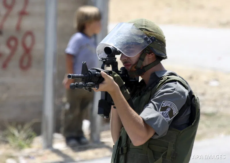 Israeli soldier points his gun at a Palestinian protestors during a demonstration against the expansion of the nearby Jewish settlement of Halamish in the West Bank village of Nabi Saleh near Ramallah, Friday, July 16, 2...