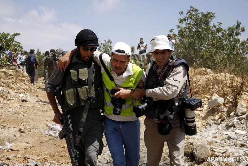 An Israeli soldier helps a wounded photographer during a demonstration against Israel's controversial separation barrier in the village of Beit Omar near Jewish settlement of Karmi zur near the West Bank city of Hebron,...