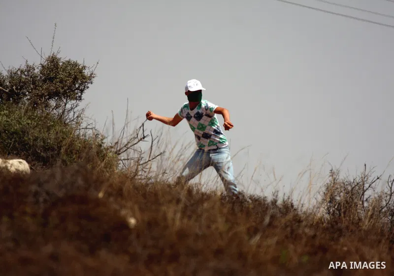 A Palestinian protester throws stones at Israeli troops, during a demonstration by Palestinian, Israeli and international activists against the expansion of the nearby Jewish settlement of Halamish in the West Bank villa...