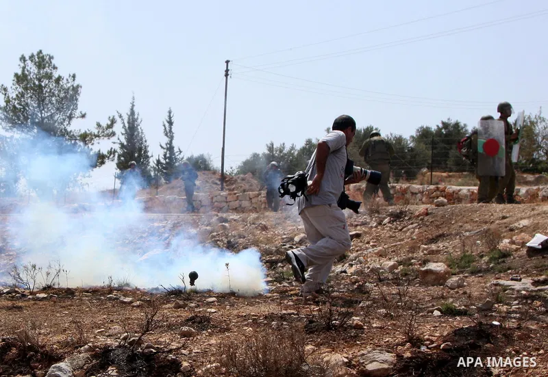 Palestinian photographer runs for cover from tear gas canister fired by Israeli soldiers during a protest against Israel's separation barrier in the West Bank village of Bilin near Ramallah, Friday, July 30, 2010. Photo...