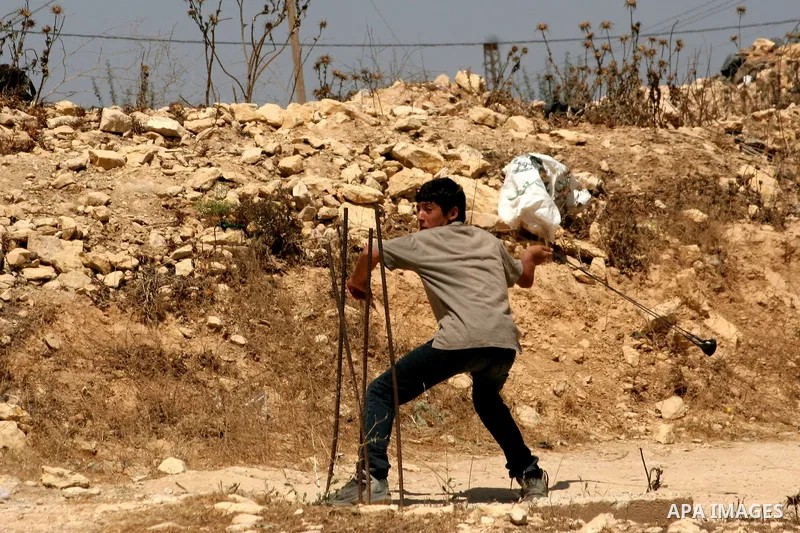 A Palestinian boy uses slingshot to throw stones at Israeli soldiers during a demonstration against Israeli settlements, in the West Bank village of Beit Omar, near Hebron, Saturday, on August 7, 2010.. Photo by Mamoun W...