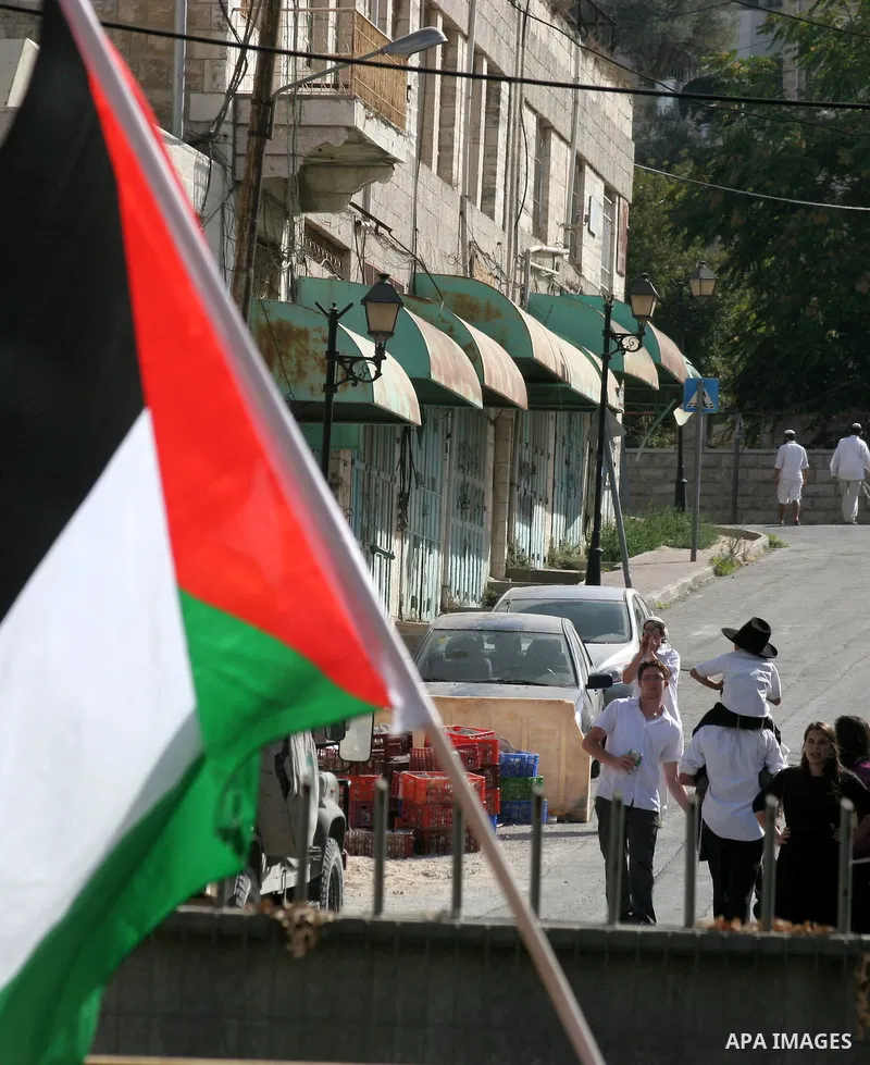 Palestinian flag flutters past Jewish settlers in the West Bank city of Hebron on August 7, 2010 during a protest by Palestinian, Israeli and foreign peace activists against Jewish settlements and the closing of Al-Shuha...