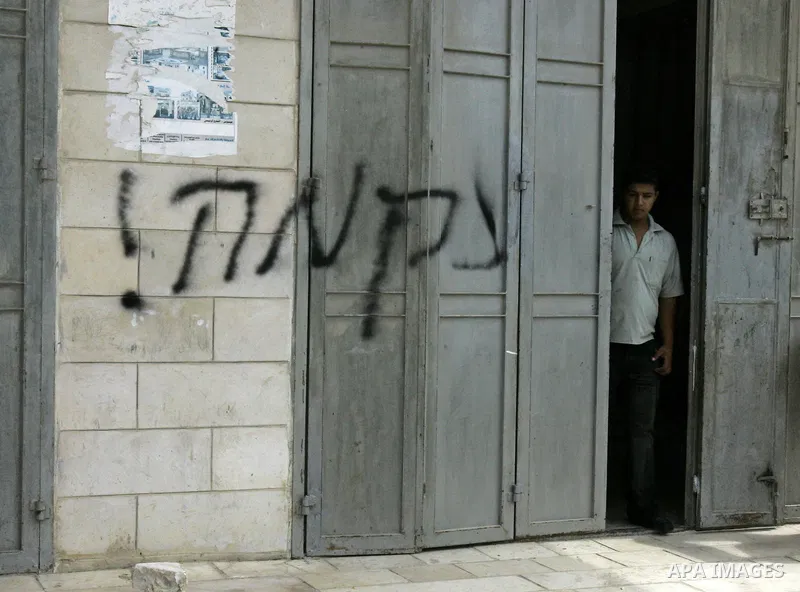 A Palestinian youth stands a building next to a graffiti, sprayed on a wall by Israeli settlers, reading 'Revenge', in Oref, near the west Bank City of Nablus on Sept. 13,2010. A car was burnt in Oref during an attack by...
