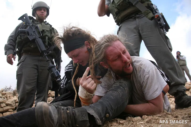 An Israeli border policeman detains a foreign protester after she was sprayed with colored pepper spray during a demonstration by Palestinian, Israeli and foreign activists against the demolishing of farm land to be used...