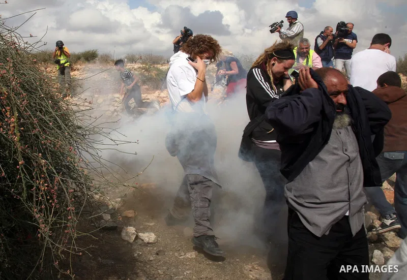 Protesters take cover from tear gas canisters fired by Israeli soldiers during a demonstration by Palestinian, Israeli and foreign activists against the demolishing of farm land to be used in the construction of Jewish s...