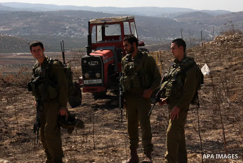 Israeli soldiers are seen in front of a crashed car at Palestinian agricultural fields during olive harvest in the West Bank village of Hawara, near Nablus on Oct. 10, 2010. Jewish settlers attacked Palestinian farmers d...
