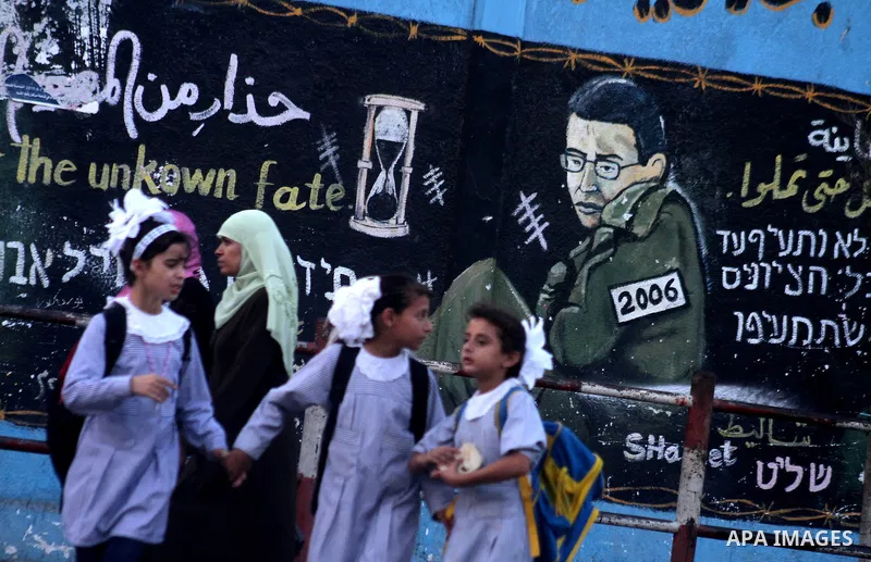 Palestinians walk in front of a wall painting showing Israeli army soldier Sgt. Gilad Schalit, in the Jebaliya refugee camp, northern Gaza Strip, Saturday, Oct. 16, 2010. The German mediator trying to broker the release...