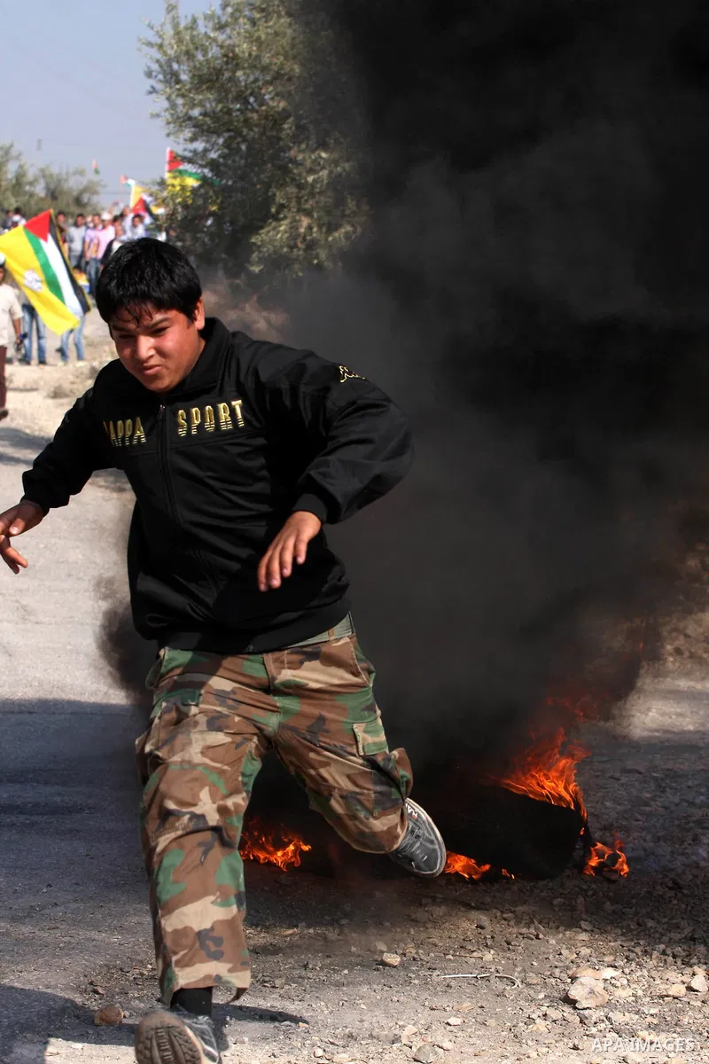 A Palestinian youth runs for cover from tear gas canister fired by Israeli soldiers during a protest against Israel's separation barrier as masked Palestinian stones throwers clash with Israeli soldiers in the West Bank...