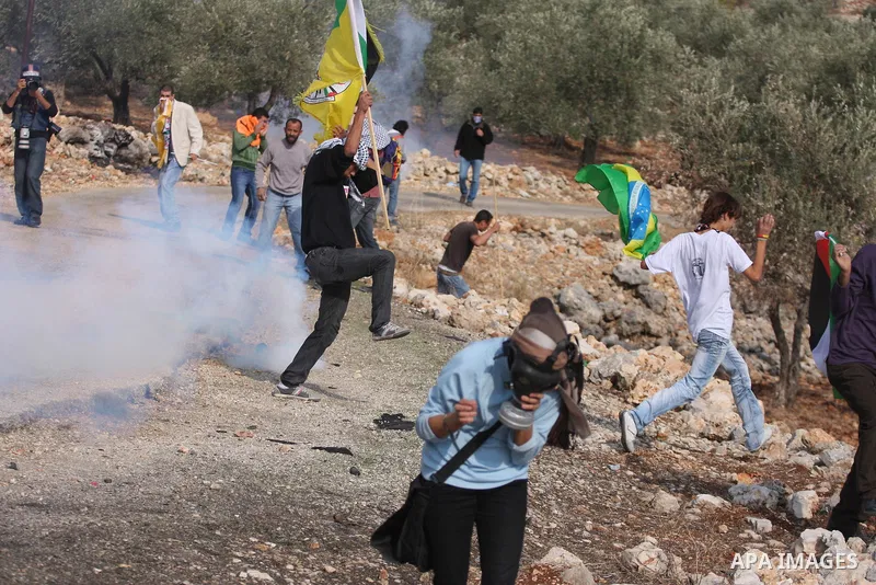 Palestinian protesters run for cover from tear gas thrown by Israeli soldiers during a protest against the construction of the Israeli controversial separation barrier in the West Bank village of Bilin near Ramallah on,...