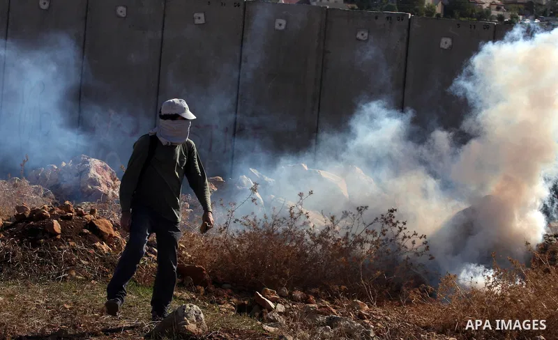 A protester runs for cover from tear gas canisters fired by Israeli soldiers during a weekly protest against Israel's separation barrier in the West Bank village of Nilin near Ramallah, Friday, Dec. 17, 2010. Israel says...