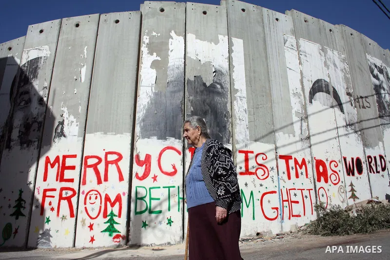 Palestinian christian woman walks past Christmas graffiti painted on the Israeli separation barrier in the West Bank town of Bethlehem, as Christmas approaches, on December 22, 2010. Photo by Najeh Hashlamoun