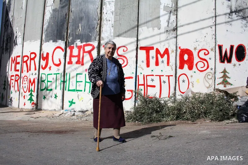 Palestinian christian woman walks past Christmas graffiti painted on the Israeli separation barrier in the West Bank town of Bethlehem, as Christmas approaches, on December 22, 2010. Photo by Najeh Hashlamoun
