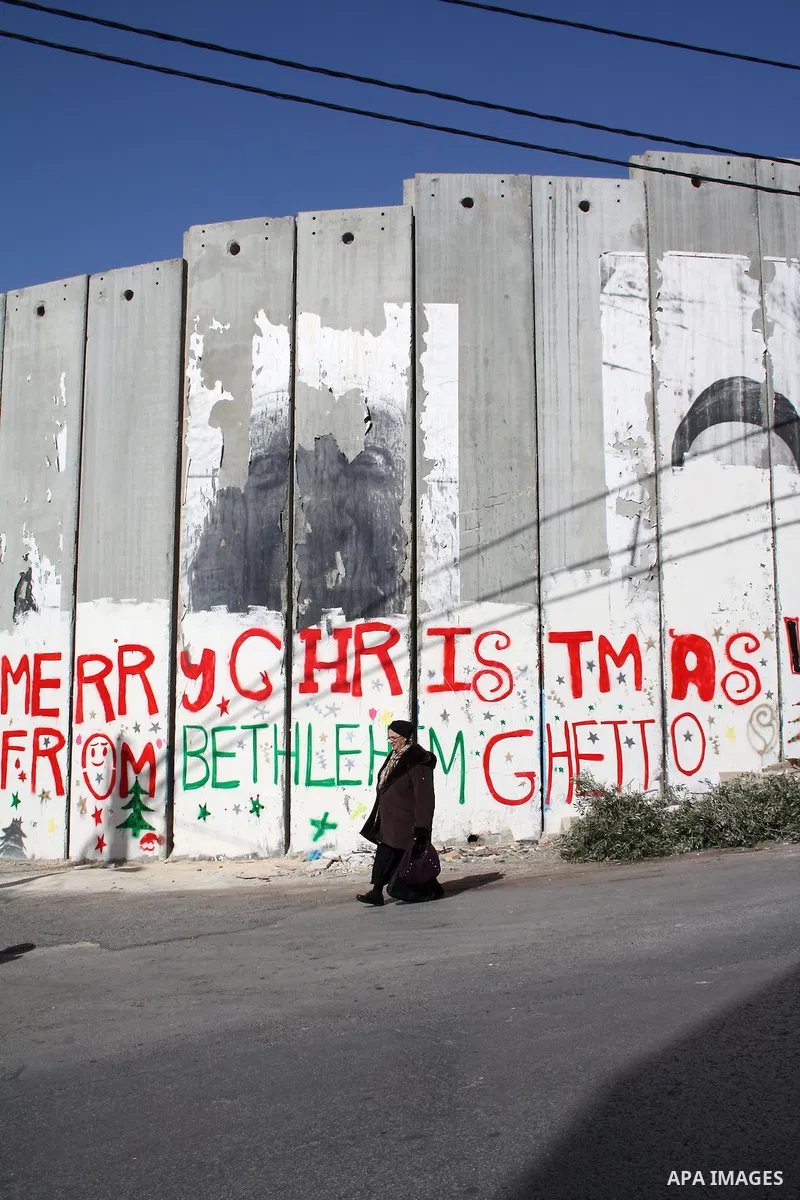 Palestinian woman walks past Christmas graffiti painted on the Israeli separation barrier in the West Bank town of Bethlehem, as Christmas approaches, on December 22, 2010. Photo by Najeh Hashlamoun
