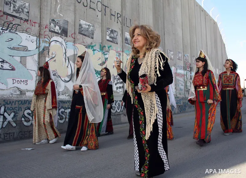 Palestinian Christian women wearing traditional clothes walk past the Israeli separation barrier in the West Bank town of Bethlehem on December 23, 2010. Scores of Christian pilgrims are preparing to gather in the tradit...