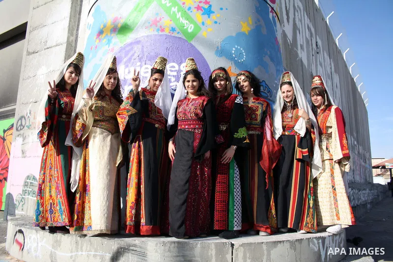 Palestinian Christian women wearing traditional clothes walk past the Israeli separation barrier in the West Bank town of Bethlehem on December 23, 2010. Scores of Christian pilgrims are preparing to gather in the tradit...